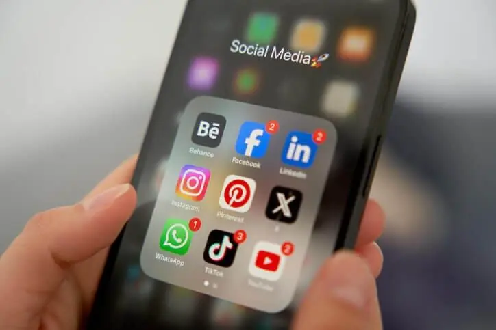Mão segura celular com pasta Social Media: Instagram, Facebook, LinkedIn, TikTok, WhatsApp e YouTube