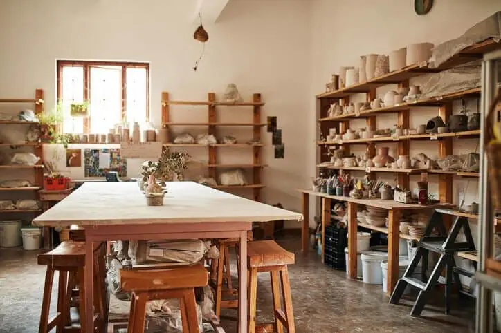 Ateliê de cerâmica com mesa de trabalho e estantes de madeira repletas de peças artesanais