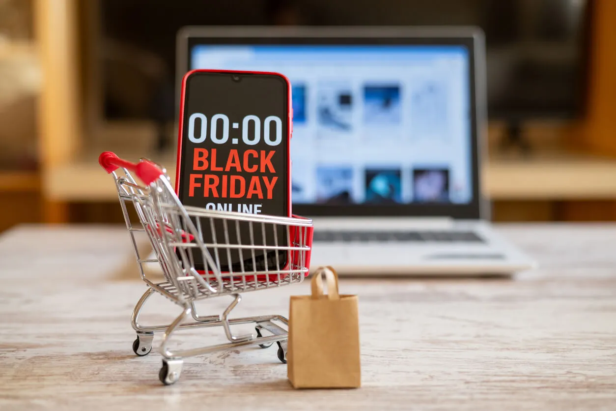 Carrinho de compras com celular exibindo a contagem regressiva da Black Friday online, ao lado de um notebook, ilustrando estratégias de marketing para a Black Friday.
