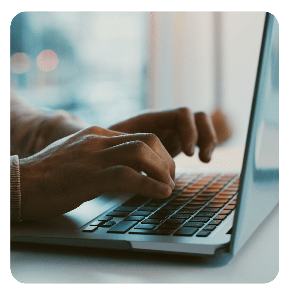 Mãos masculinas digitando em um notebook, em um ambiente com fundo desfocado, sugerindo trabalho ou navegação online.