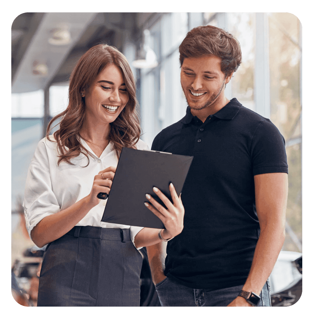 Mulher e homem sorrindo enquanto analisam um documento em uma prancheta, em um ambiente corporativo ou de vendas, sugerindo consultoria ou negociação.