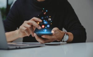 Pessoa usando smartphone em uma estratégia para redes sociais, com ícones de interação e engajamento.