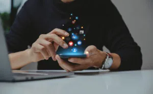 Pessoa usando smartphone em uma estratégia para redes sociais, com ícones de interação e engajamento.